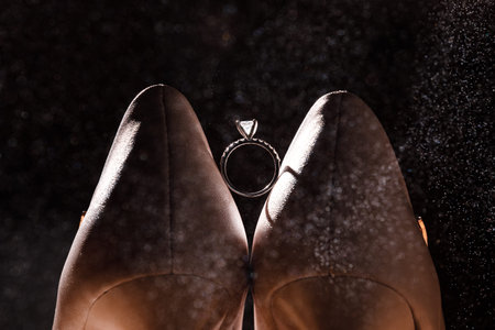Golden ring with diamond between pair of white shoes on dark background.