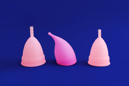 three different pink reusable silicone menstrual cup isolated on blue background. Concept of...