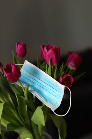 Coronavirus covid 19 quarantine concept. Easter spring tulip flowers with face medical mask on the table. copy space. selective focus.の写真素材
