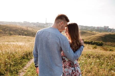 beautiful young couple hugging in a field with grass at sunset. stylish man and woman having fun outdoors. family concept. copy spaceの写真素材