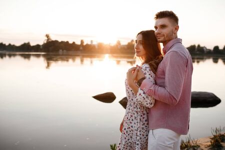loving couple hugging on the lake at sunset. Beautiful young couple in love walking on the shore of the lake at sunset in the rays of bright light. copy space.の写真素材