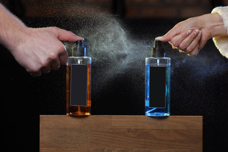 the hands of a man and a woman spray a colored hair lotion. two spray cans on black background on...