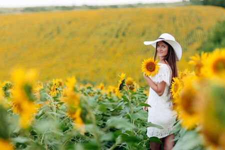 Woman in the field of sunflowers. A happy, beautiful young girl in a white hat is standing in a large field of sunflowers. Summer time. Back viewの写真素材