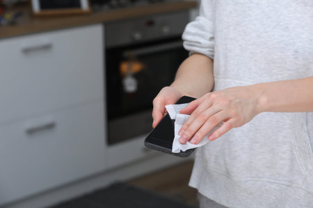 Woman disinfecting phone with antiseptic wet wipe. Antiseptic napkin to prevent spread of germs,...