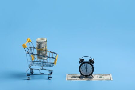 shopping time. Alarm clock and dolar on blue background. time is money. Time management concept. money in the basket. selective focus. place for text.の写真素材