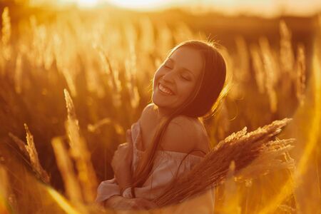 Beautiful carefree woman in fields being happy outdoors. Outdoor atmospheric lifestyle photo of young beautiful lady. Brown hair and eyes. Warm autumn. Warm springの写真素材