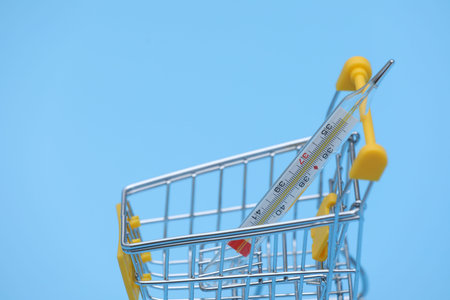 close-up of shopping trolley on blue background with thermometer. Medicine concept with copy space