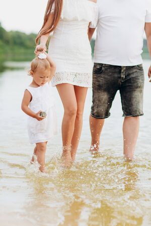 Mom, dad, daughter walking on stone near lake. View down. Bottom view of legs. The concept of summer holiday. Mother's, father's, baby's day. Family spending time together on nature. Family lookの写真素材