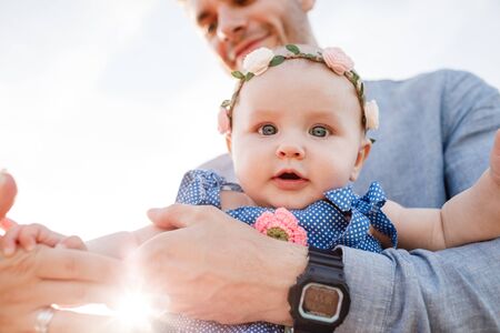 Young handsome father holds little daughter in his hands and smiles on sunny day. Happy family. Father's day concept. Dad raise up her daughter. Little baby smilingの写真素材