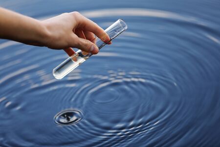 Water sample. Hand collects water to explore. Concept - water purity analysis, environment, ecology. Water testing for infections, permission to swim. selective focus, place for textの写真素材