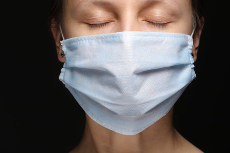 a woman's face in a medical mask on black background, an outbreak of coronavirus infection and...