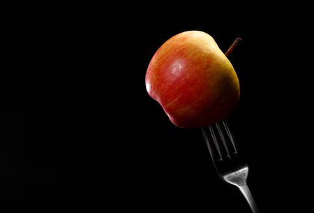 Healthy diet. Weight control. Apple on fork against black background. Healthy food concept. One ripe organic, juicy, fragrant apple with a metal fork, close-up.の写真素材