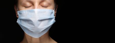 Close-up banner of a young woman with close eyes a medical mask on black background. Quarantine, coronavirus epidemic pandemic, covid-19. Stay home concept. Virus protection. copy spaceの写真素材