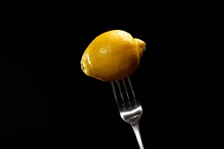 fresh lemon on the metal fork on a black background. Fresh tropical fruit, yellow citrus, flat layer, space for text.の写真素材