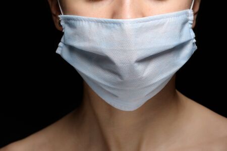 Protection against contagious disease, coronavirus. Female is wearing hygienic face surgical medical mask to prevent infection, respiratory illness as flu, 2019-nCoV. Studio photo black background.の写真素材