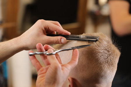 Men's hairstyling, haircutting, in a barber shop or hair salon. Close-up of man hands grooming kid boy hair in barber shop. Portrait of male child at the barber shop to cut his hairの写真素材