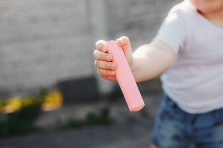 Closeup of child holding pink chalk for drawing. Outdoor entertainment. drawing on paving. selective focusの写真素材