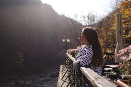 young beautiful woman enjoys the view of the mountain river and shows the tongue on the terrace of a...