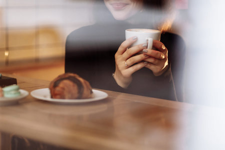 Young woman holding in hands hot aroma coffee or tea with croissant in breakfast time at cafe. cropped photo.の写真素材