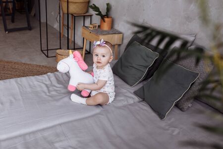 adorable little girl is playing with toy unicorn on bed at home. concept of childhood day. happy babys, family dayの写真素材