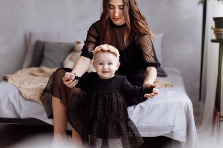 Beautiful young woman and her charming little daughter are hugging and smiling on bed at studio.の写真素材