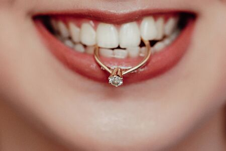 Close up young bride showing her wedding ring holding in teeth and smiling. woman with diamond ring and red lipsの写真素材