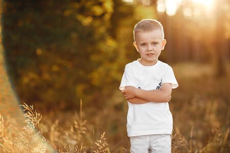 Portrait of little boy with blond hair and a white shirt near. portrait at sunsetの写真素材