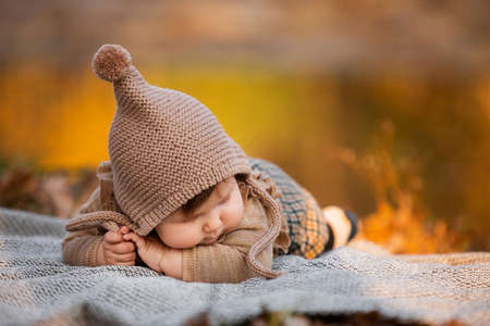 Beautiful baby girl sitting on the plaid near pond. Child outdoor. Baby at picnic in autumn park on sunny day. Pretty little girl.の写真素材