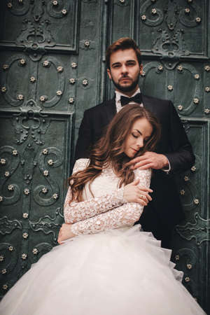 Wedding couple hugging in the old city. Blue vintage doors and cafe in ancient town on background. stylish bride in white long dress and groom in suit and bow tie. wedding day.の写真素材