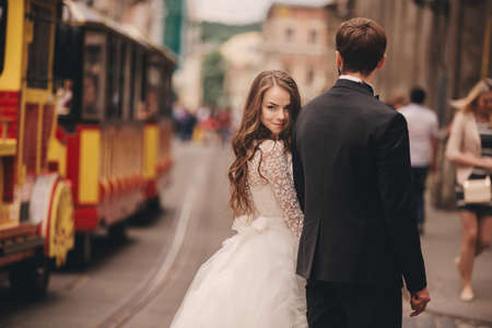 Beautiful newlyweds hugging near the ancient door. Wedding portrait of a stylish groom and a young bride near old house in in a European town.の写真素材