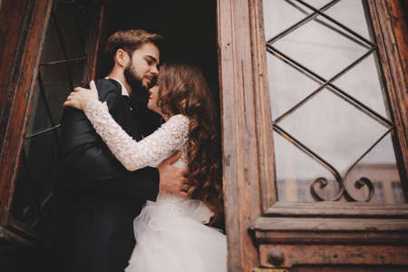 Happy newlywed couple hugging and kissing in old European town street, gorgeous bride in white wedding dress together with handsome groom. wedding day.の写真素材