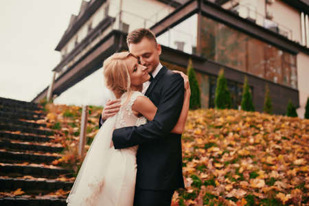 portrait of Happy young married couple in golden yellow fall autumn park. beautiful bride and stylish groom hugging in wedding day.の写真素材