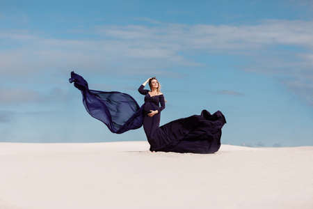 Beautiful young pregnant woman wearing black dress walking at the beach. Future mother conceptの写真素材
