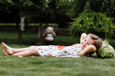 A cute little girl is playing with her pet dog outdooors on grass at home.の写真素材