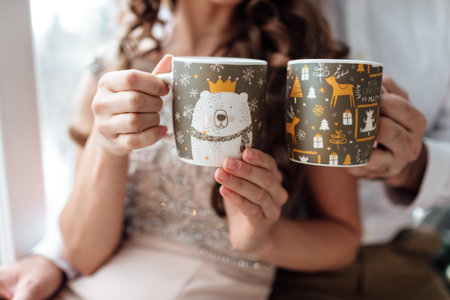 Christmas. Love. Home. hands of man and woman are holding with christmas decorations cups with hot...