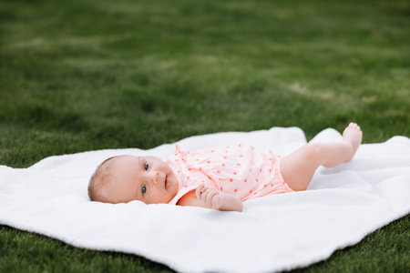 Newborn baby girl on grass in the park outdoors, lies on a white blanket looking around. selective...