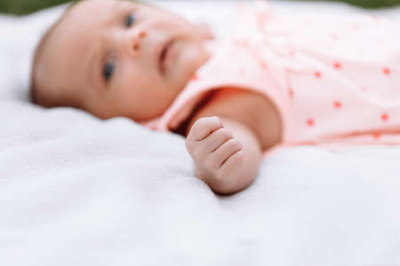 Newborn baby girl on grass in the park outdoors, lies on a white blanket looking around. selective focusの写真素材