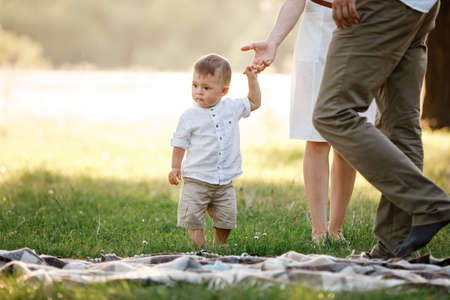 Happy adorable baby boy walks on the grass in the park on summer day. Happy smile. Child in trendy and cute clothes.の写真素材