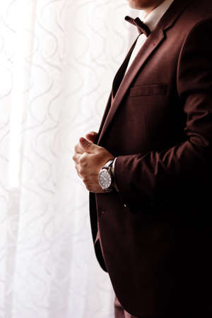 man in an elegant brown tuxedo with a silk bow tie and a watch. selective focusの写真素材