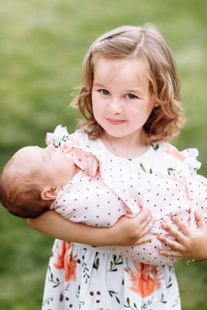 cute little girl holding her younger newborn sister outdoors. Relations between relatives. Two sisters love each other's. family lifestyle.の写真素材
