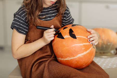 little girl paints a pumpkin for Halloween. preparation for halloween. Halloween holiday and family lifestyle background. selective focus.の写真素材