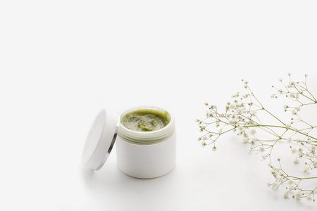 Opened plastic container with cream and flowers on a white background. face cream. herbal cream. cosmetic productsの写真素材