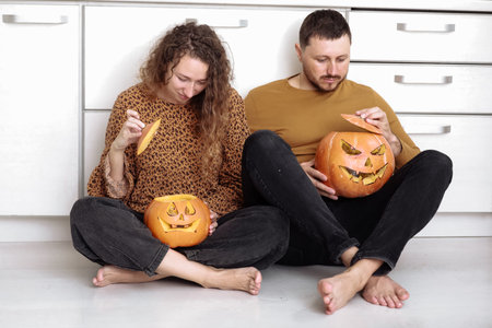 Young couple man and woman sitting on the floor at kitchen at home having fun and preparing for halloween talking laughing cheerful.の写真素材