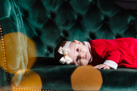 Cute baby girl in red bow on head and white sweater lying on blanket, a Christmas background in a...