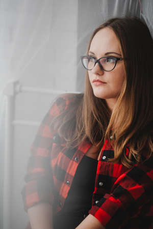 girl in glasses and a black dress in a red chair on a background of a black wall.の写真素材