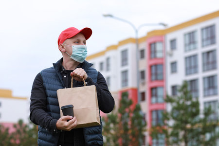 Delivery man in red cap, face medical mask hold empty cardboard box outdoors. Service coronavirus....