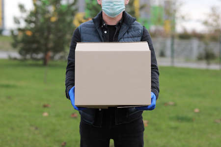 Delivery man in red cap, face medical mask and gloves hold paper bag near the car outdoor. Service coronavirus. Online shopping. mock upの写真素材
