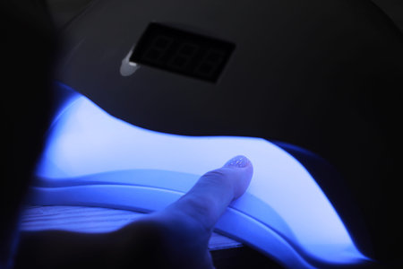 Closeup view of female hands with gel polish manicure. Woman puts hand into led uv lamp for curing...