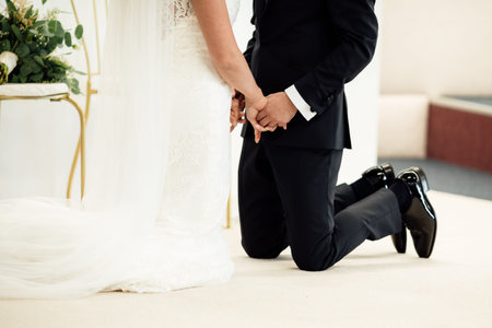 newlyweds standing on their knees holding hands and closed their eyes.の写真素材