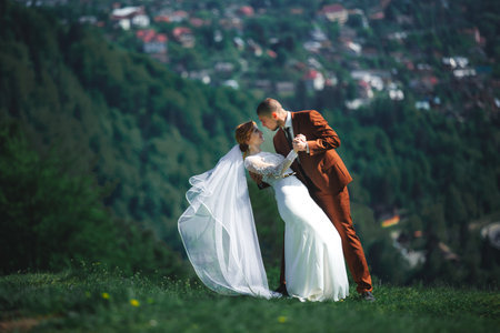 Happy stylish couple newlyweds in the green forest on summer day. bride in long white dress and groom in red suit are hugging. wedding day.の写真素材